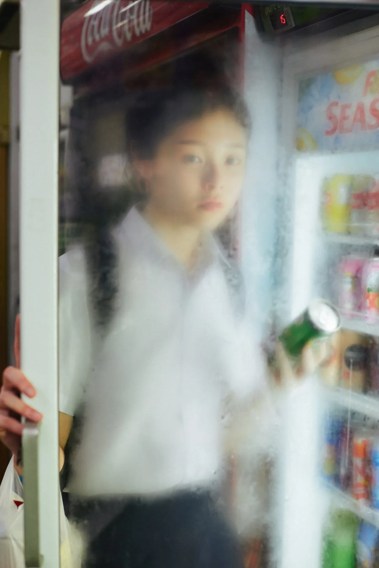From Shavonne Wong and Lenne Chai's By Proxy series, a young woman behind a fogged fridge door, blending physical space and virtual identity in a nostalgic Singapore setting.