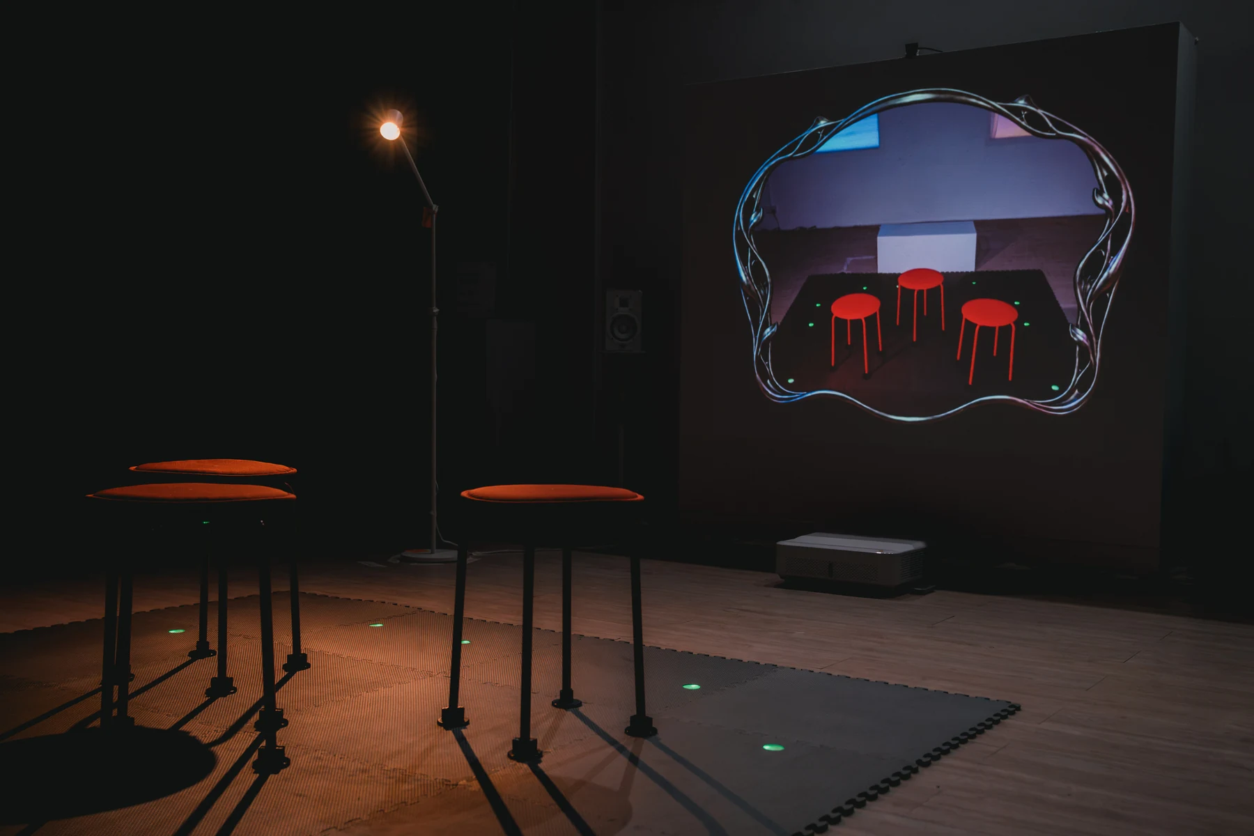 Three stools on a tracked floor mat face a large projection in the empty installation room.