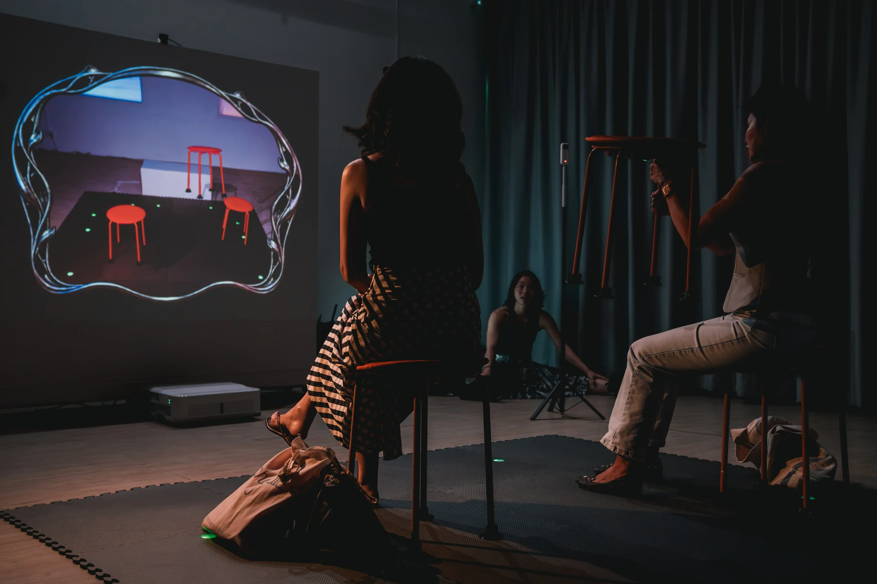 A participant holds a stool on the right while a projection on the left shows the stool without its holder.